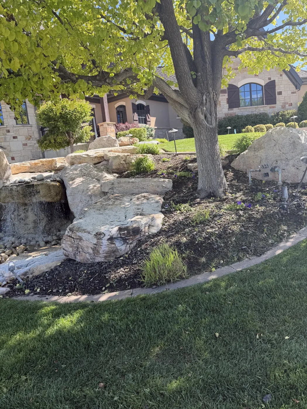 Refreshed planting bed around a boulder waterfall